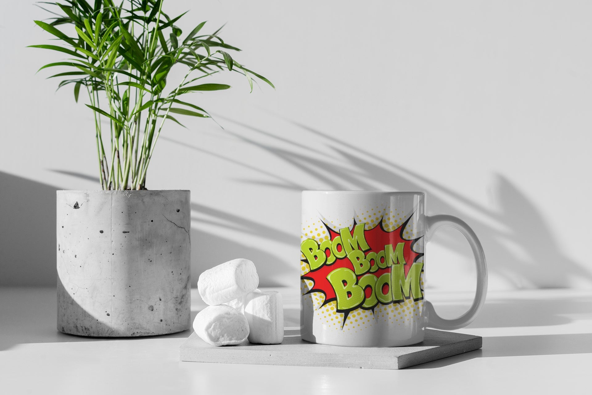 Mug with colorful text design next to a potted plant on a light surface.