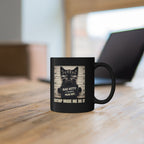 Black mug with a cat graphic and text on a wooden surface