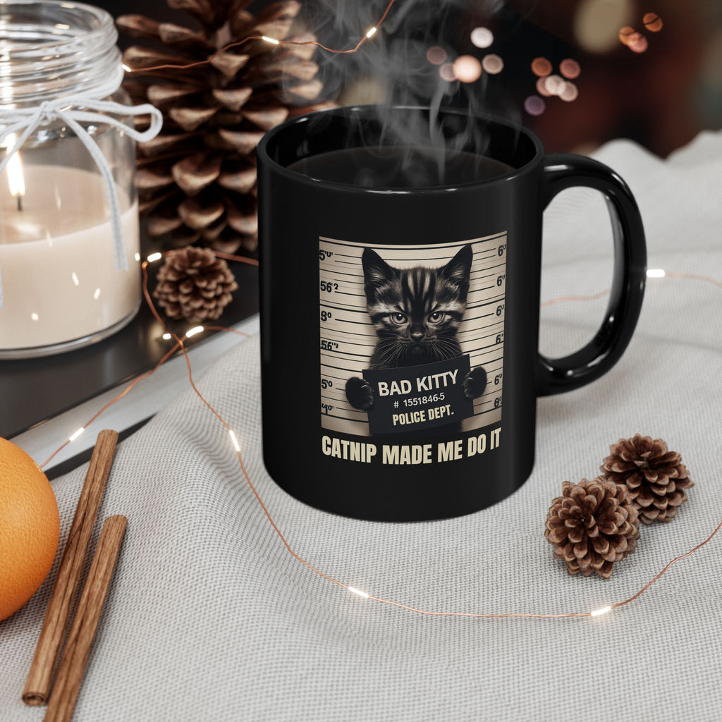 Black mug with a cat graphic and text, surrounded by decorative items on a table.