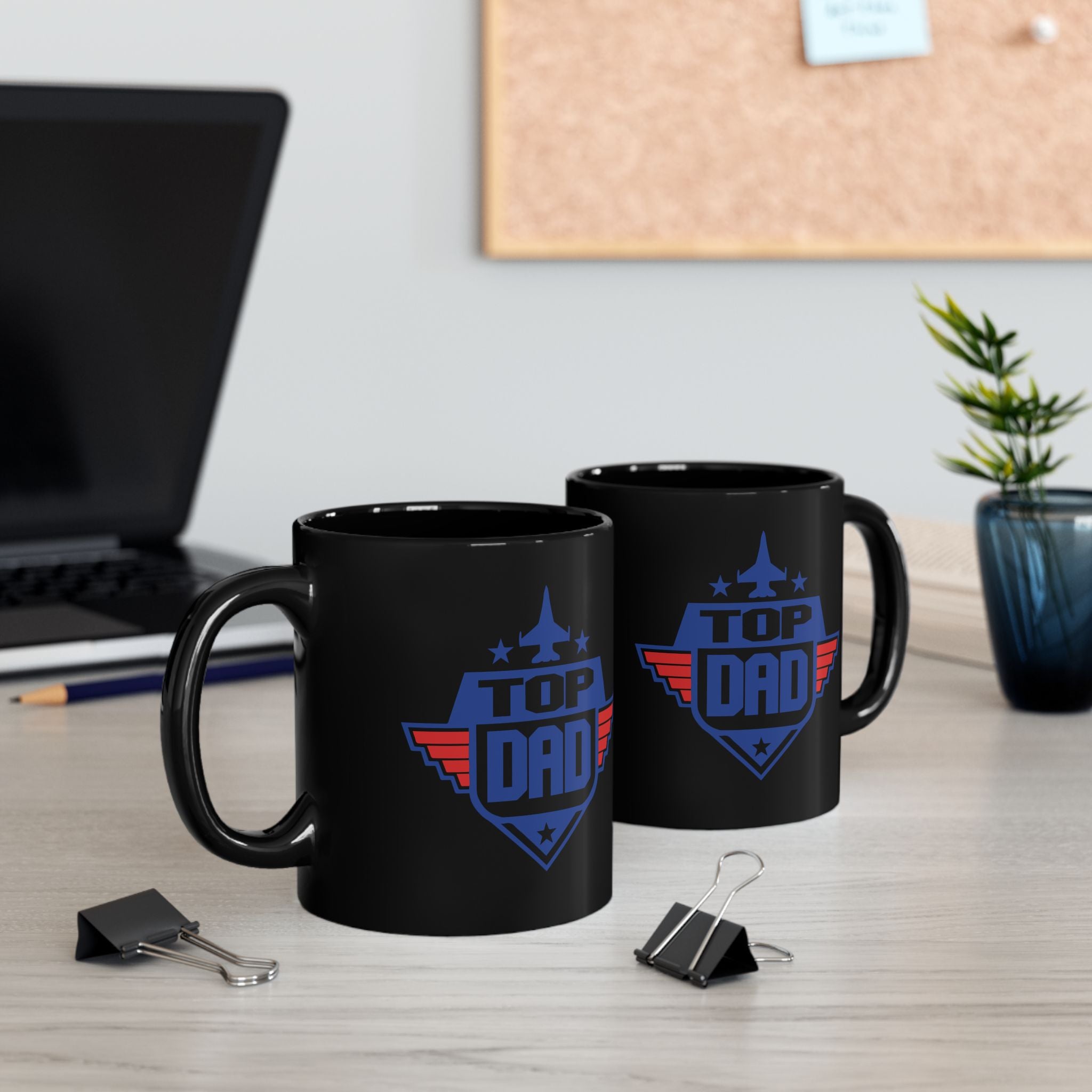 Two black mugs with 'Top Dad' design on a desk with office items.