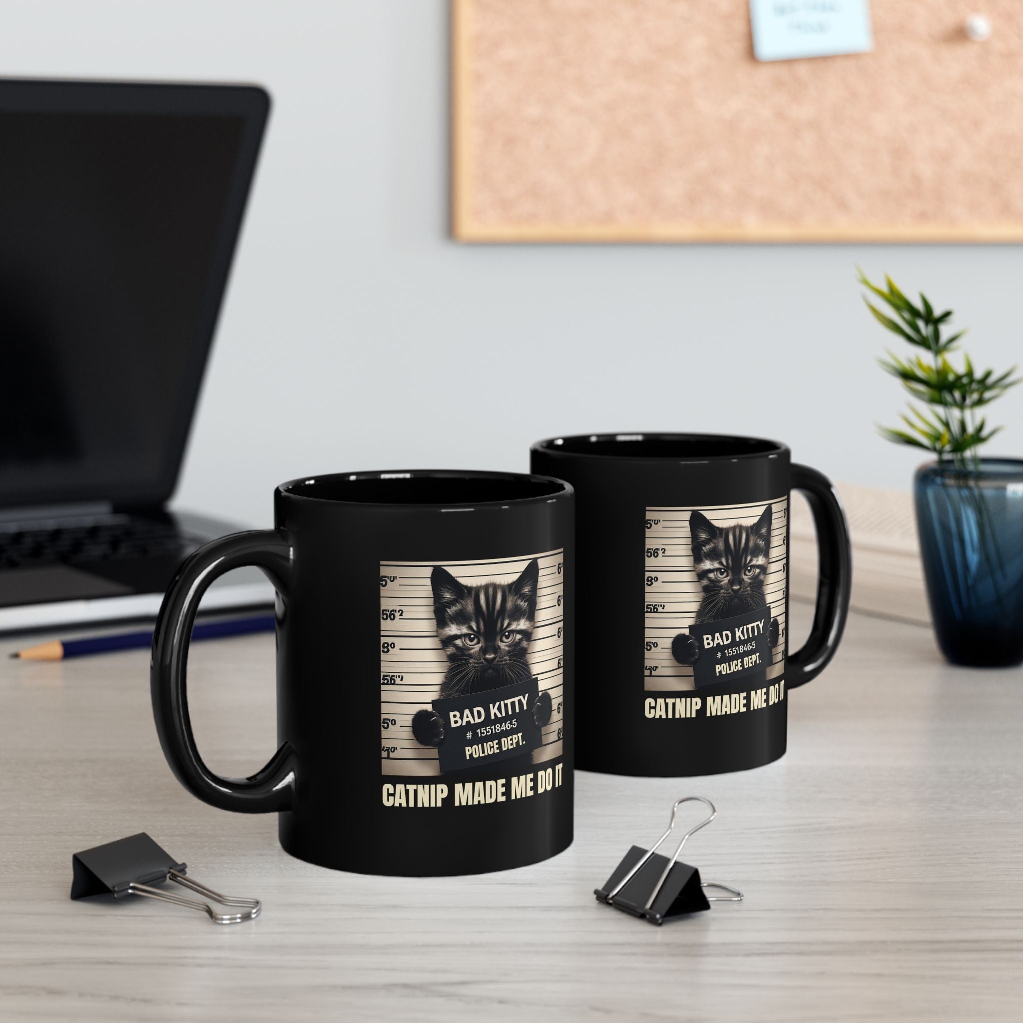 Two black mugs with cat-themed designs on a desk with office items.