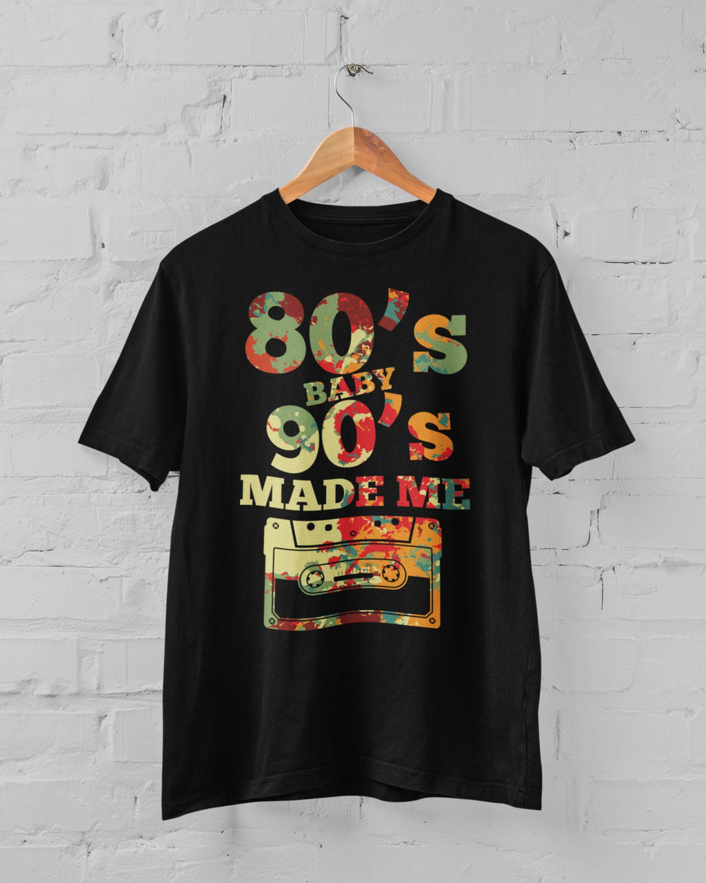 Black t-shirt with colorful text and cassette tape graphic on a hanger against a white brick wall.