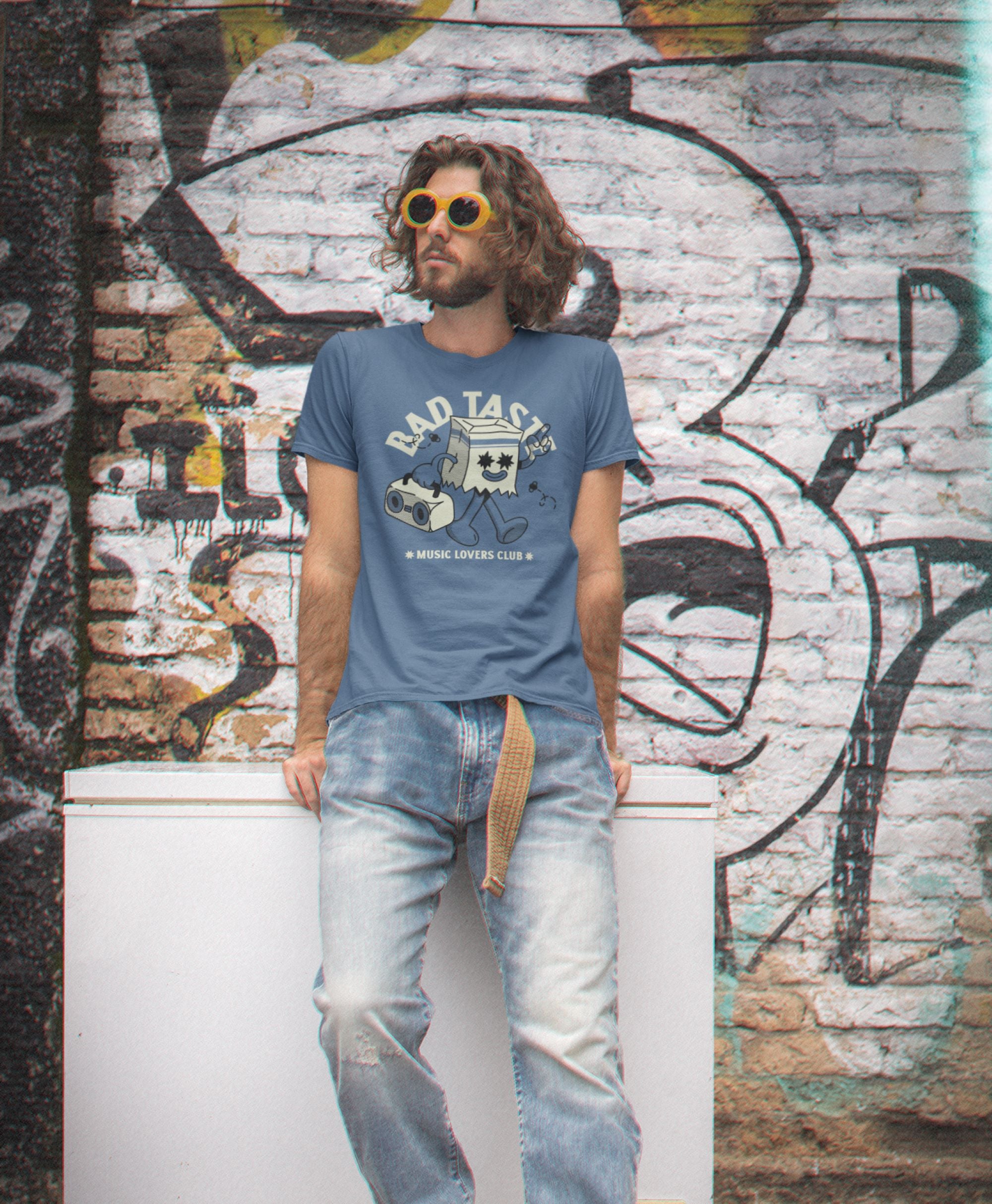 Man wearing a blue t-shirt with graphic design and text, standing against a graffiti-covered wall.