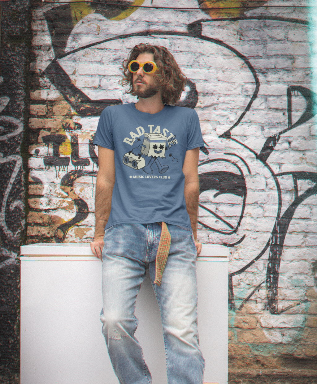 Man wearing a 'Bad Taste' t-shirt in front of a graffiti-covered wall