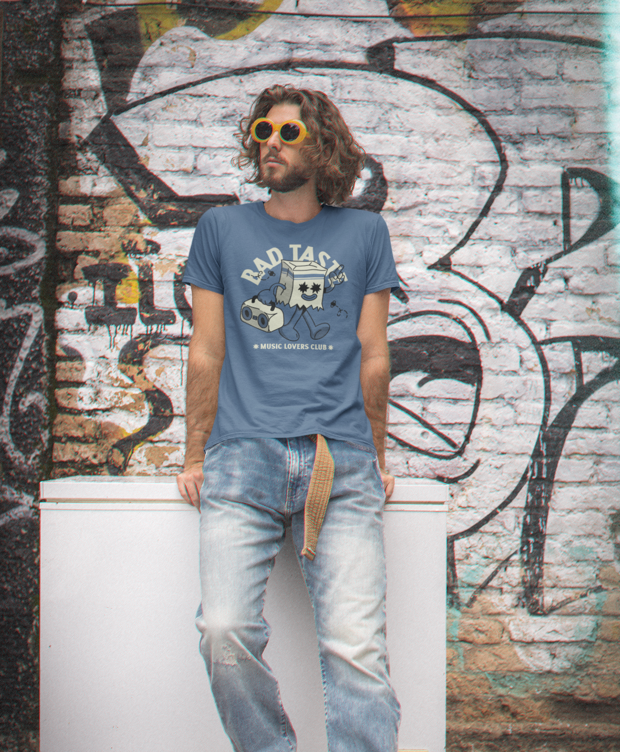 Man wearing a 'Bad Taste' t-shirt in front of a graffiti-covered wall