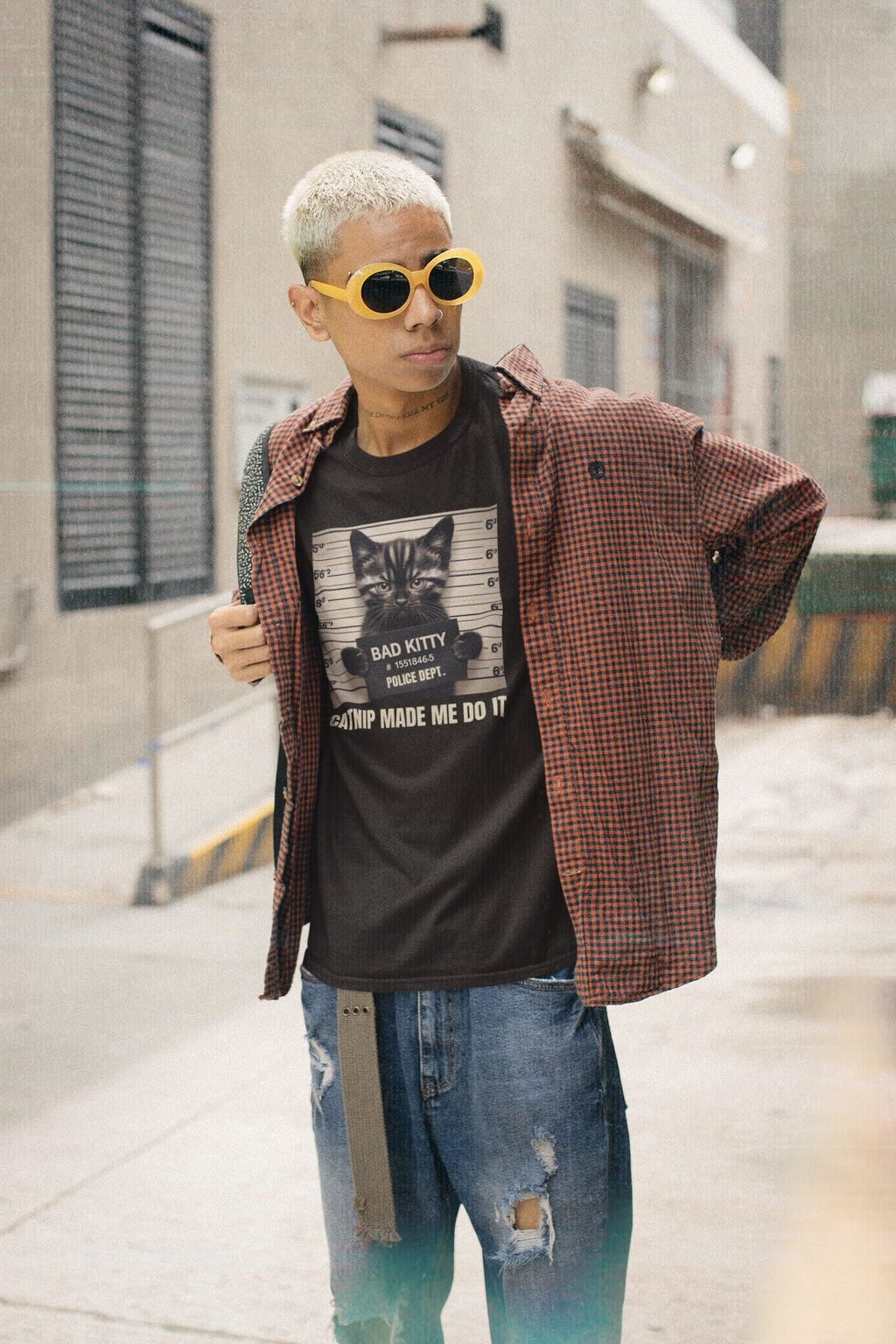 Person wearing a graphic t-shirt, plaid shirt, and sunglasses on a city street.