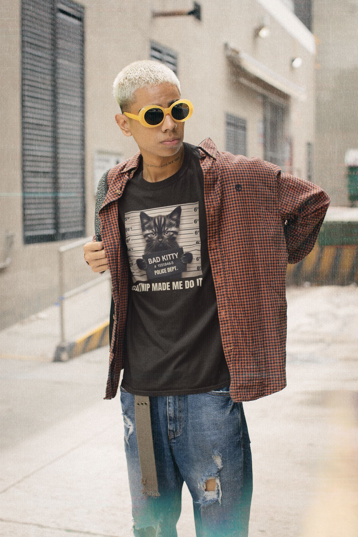 Person wearing a graphic t-shirt, plaid shirt, and sunglasses on a city street.