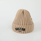 Beige knit beanie with 'Boston, 1630' text on a light gray background