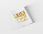 A white rectangular card or poster with metallic gold foil text reading 'I MATCH Energy' and smaller text below, shown at an angle on a light gray background with a soft shadow.
