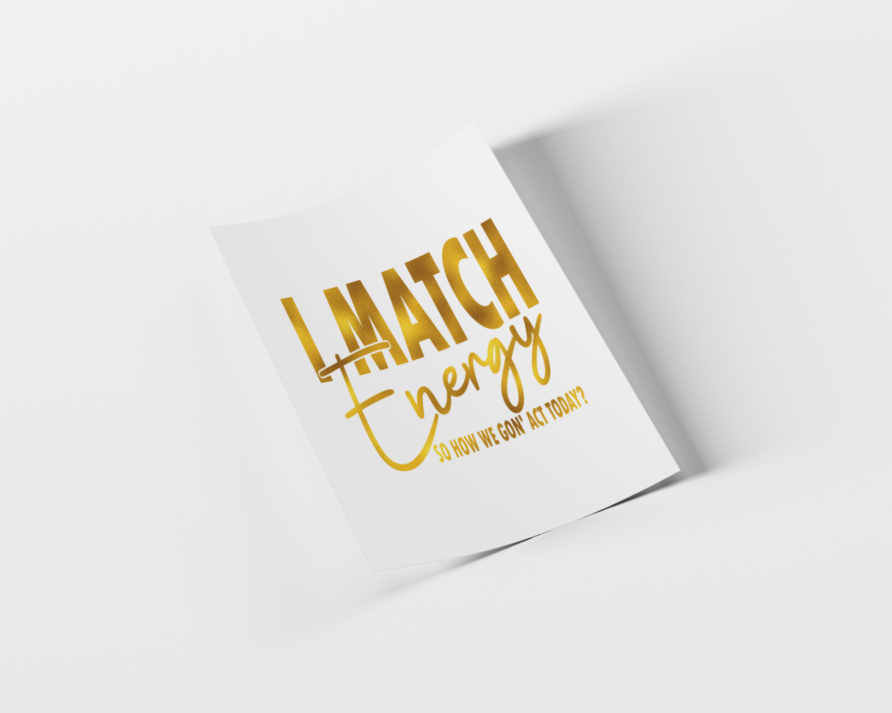 A white rectangular card or poster with metallic gold foil text reading 'I MATCH Energy' and smaller text below, shown at an angle on a light gray background with a soft shadow.