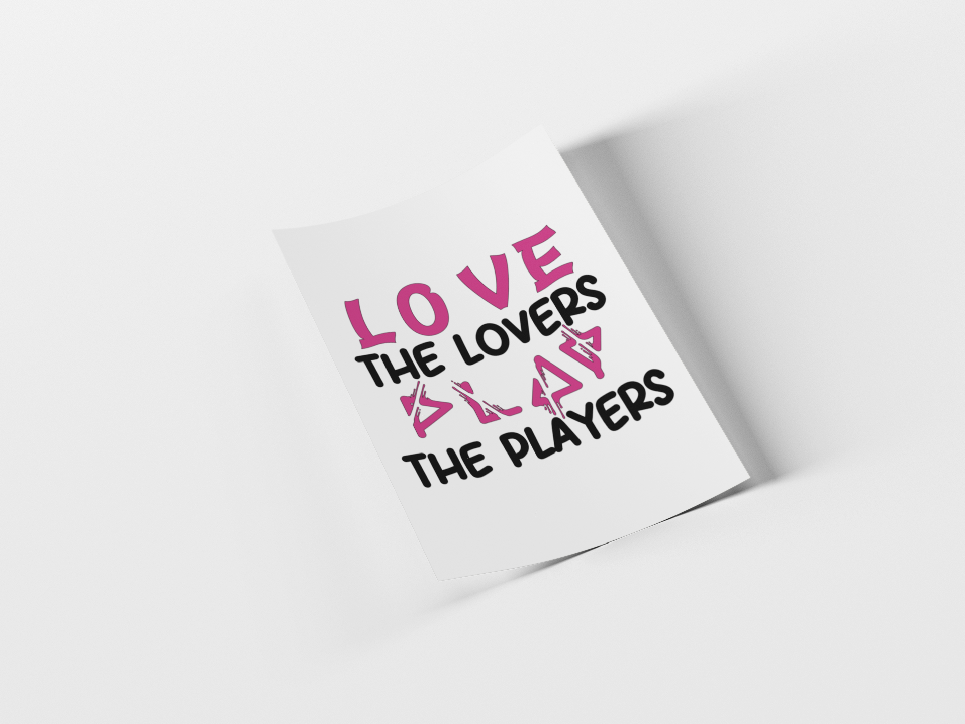 A white rectangular card or poster shown at an angle on a light gray background, printed with the phrase “LOVE THE LOVERS PLAY THE PLAYERS” in pink and black text.
