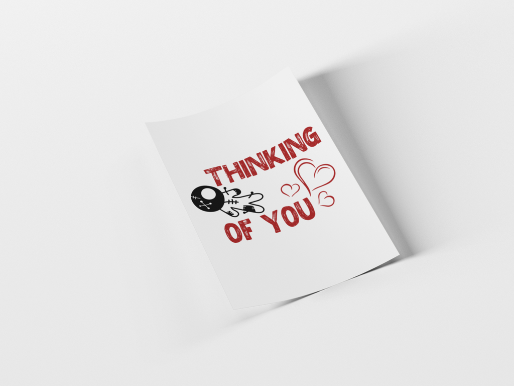 A white greeting card or paper print shown at an angle on a light gray background, printed with the phrase 'THINKING OF YOU' in red and a small black skull-and-crossbones graphic with hearts.