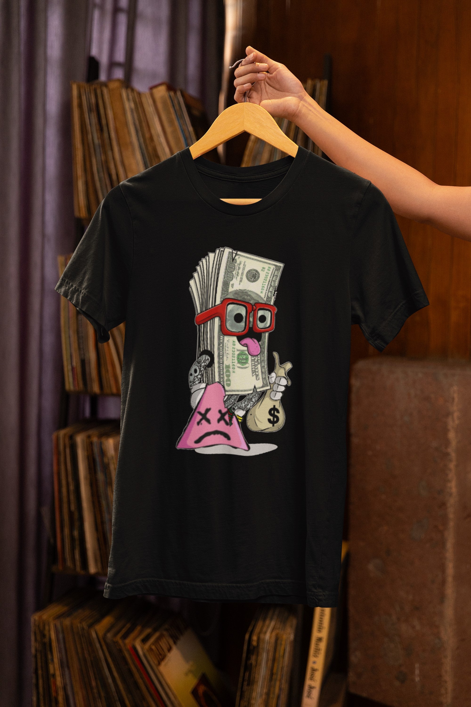 Black t-shirt with a colorful graphic design on a hanger against a bookshelf background