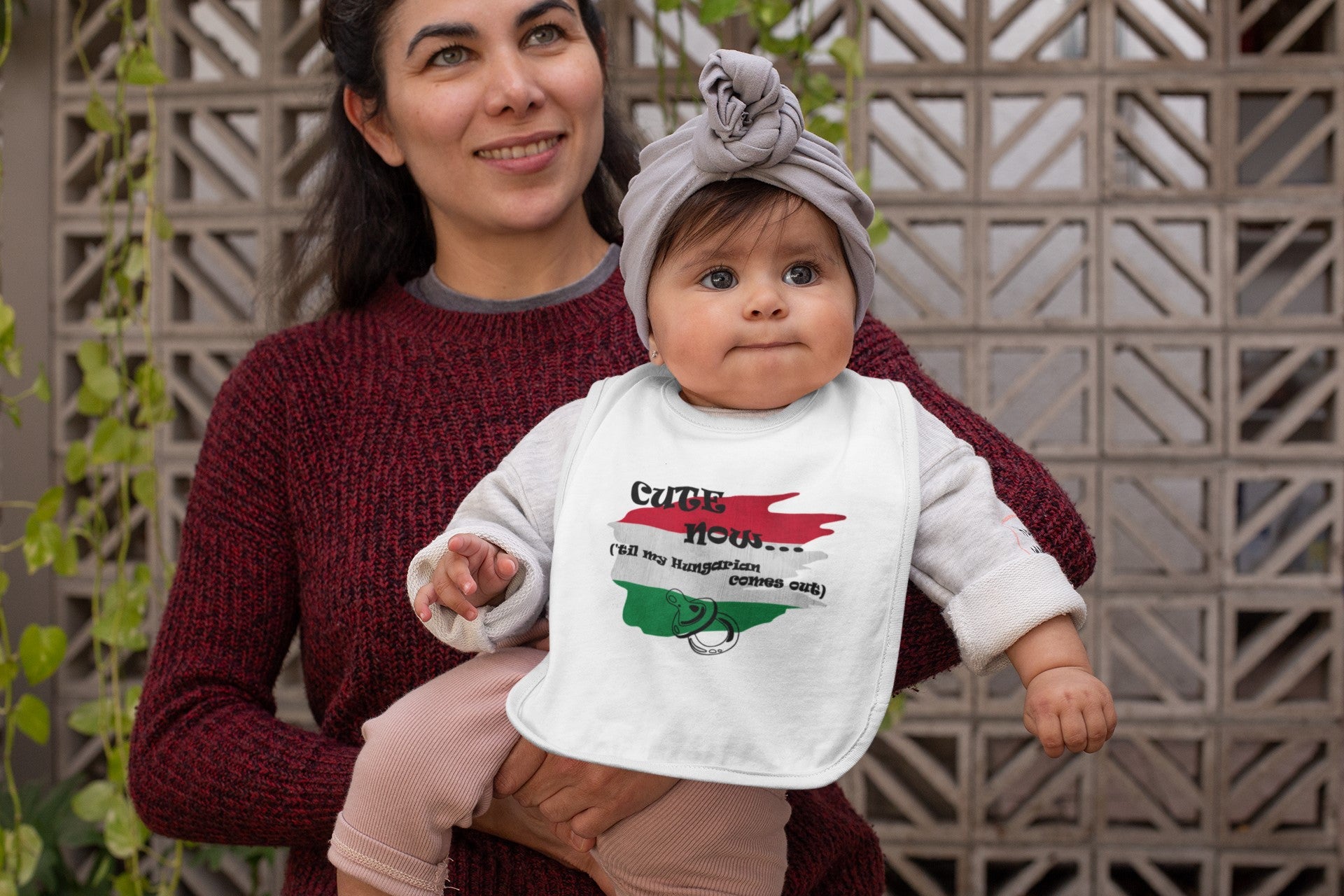 Woman holding a baby wearing a bib with text and a flag design.