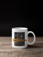 A white ceramic coffee mug with a graphic print of a soldier in a gas mask and the text 'DUTY IS CALLING' in yellow, set on a wooden surface against a black background.