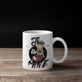 A white ceramic coffee mug with a custom graphic print of a French Bulldog holding a football and the text 'This is Mine', displayed on a wooden surface against a solid black background.