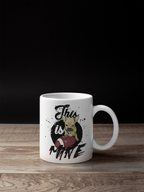 A white ceramic coffee mug with a custom graphic print of a French Bulldog holding a football and the text 'This is Mine', displayed on a wooden surface against a solid black background.