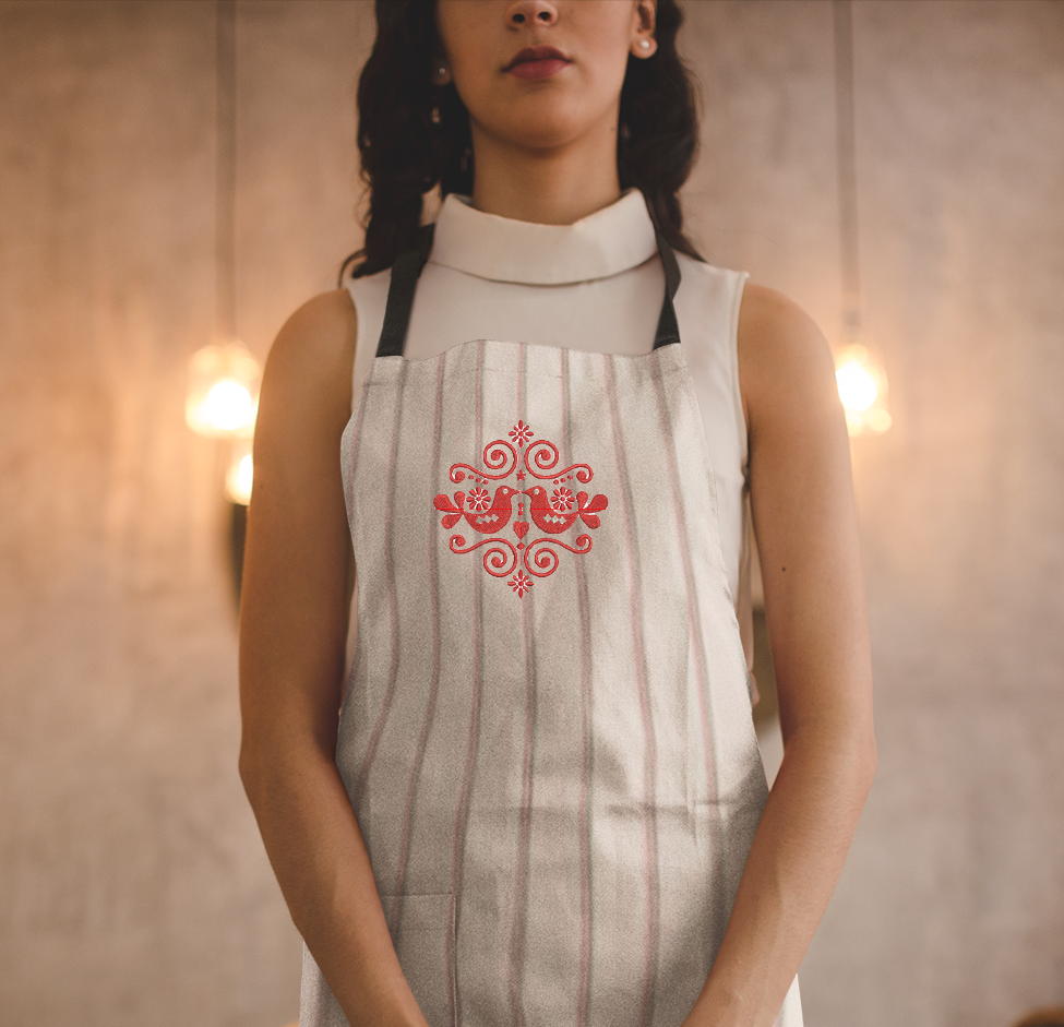 Person wearing a white apron with red floral design in a warm-toned room.