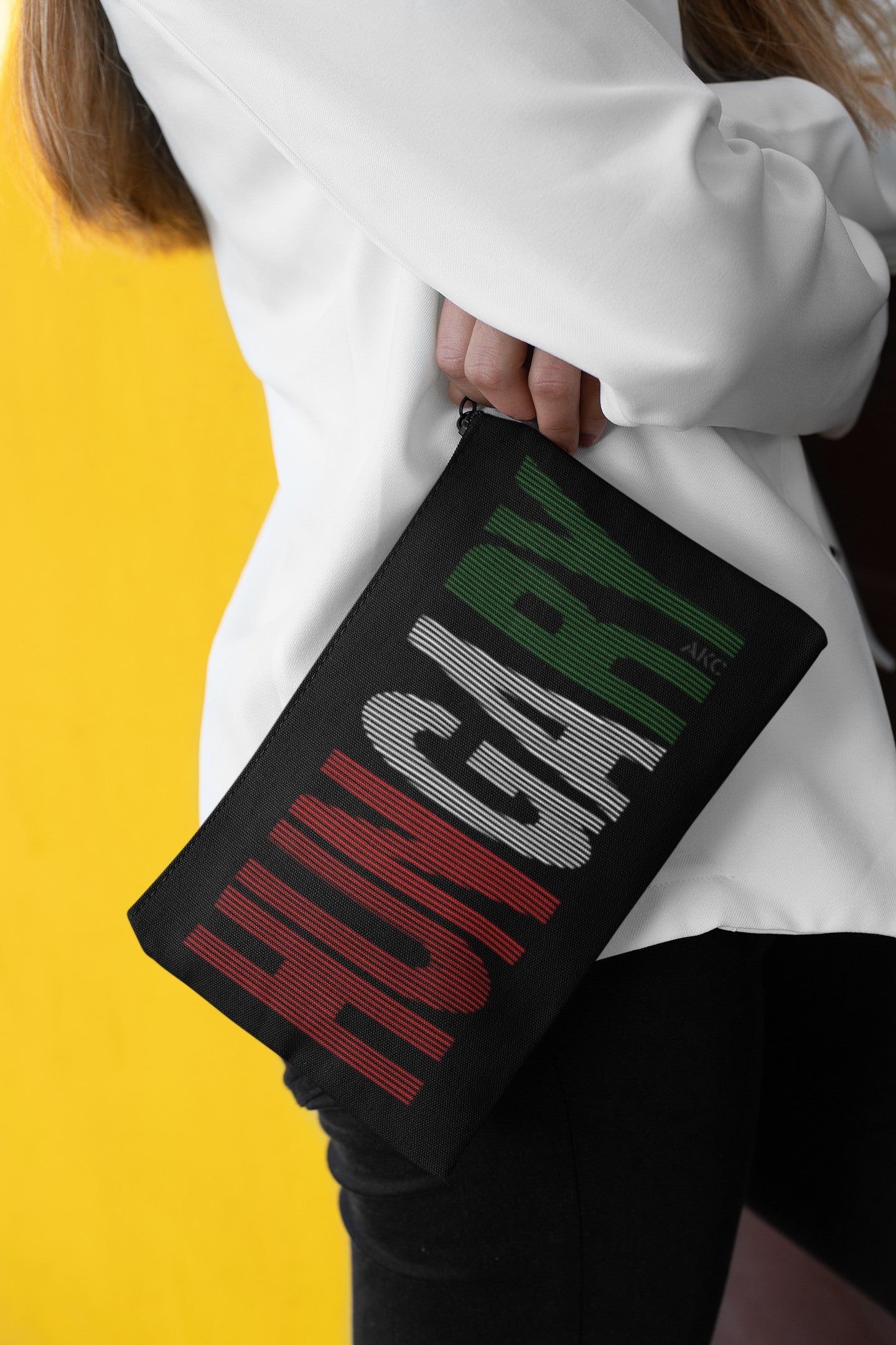 Person holding a black pouch with 'HUNGARY' printed in colorful letters against a yellow background