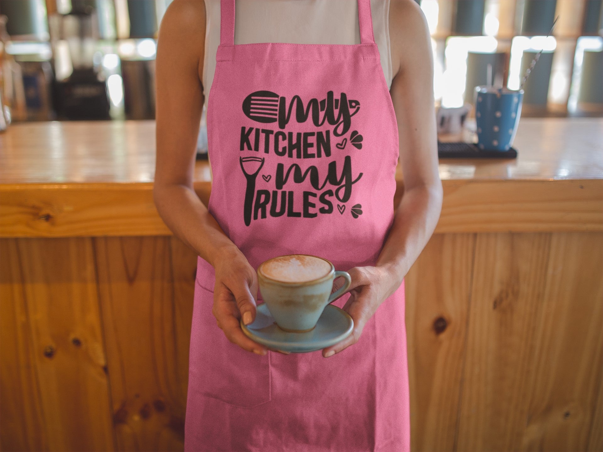 Person wearing a pink apron with 'My Kitchen My Rules' text, holding a cup of coffee.