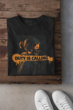 Black t-shirt with 'Duty is Calling' graphic on a wooden surface with white sneakers.