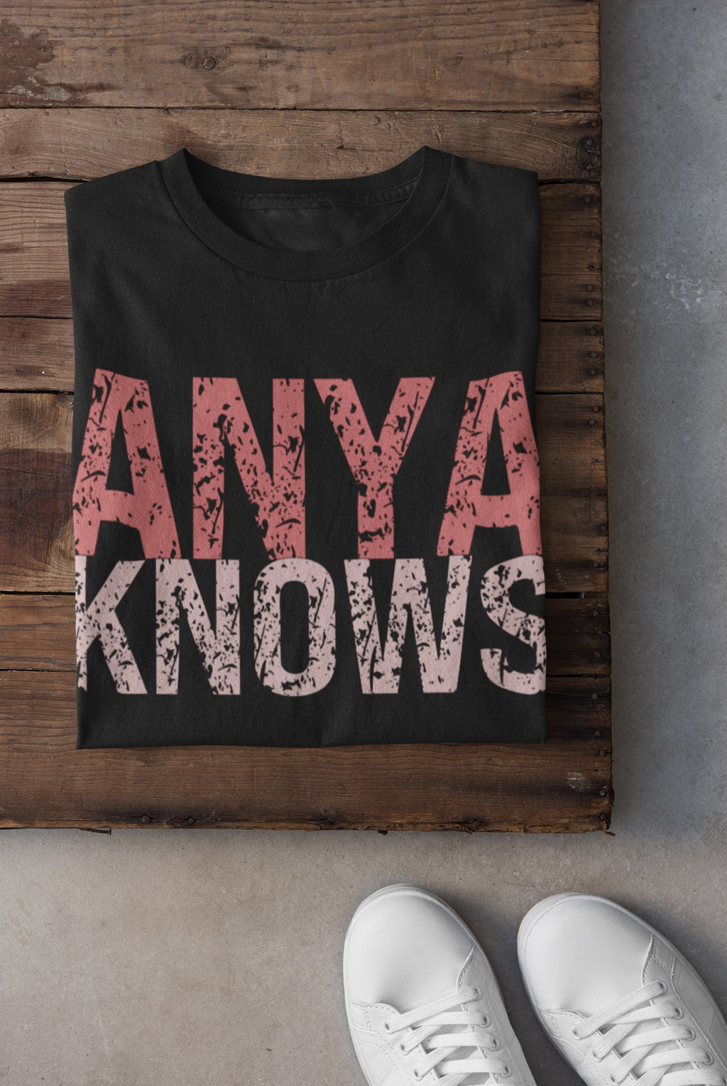 Black t-shirt with 'ANYA KNOWS' text on a wooden surface with white sneakers.