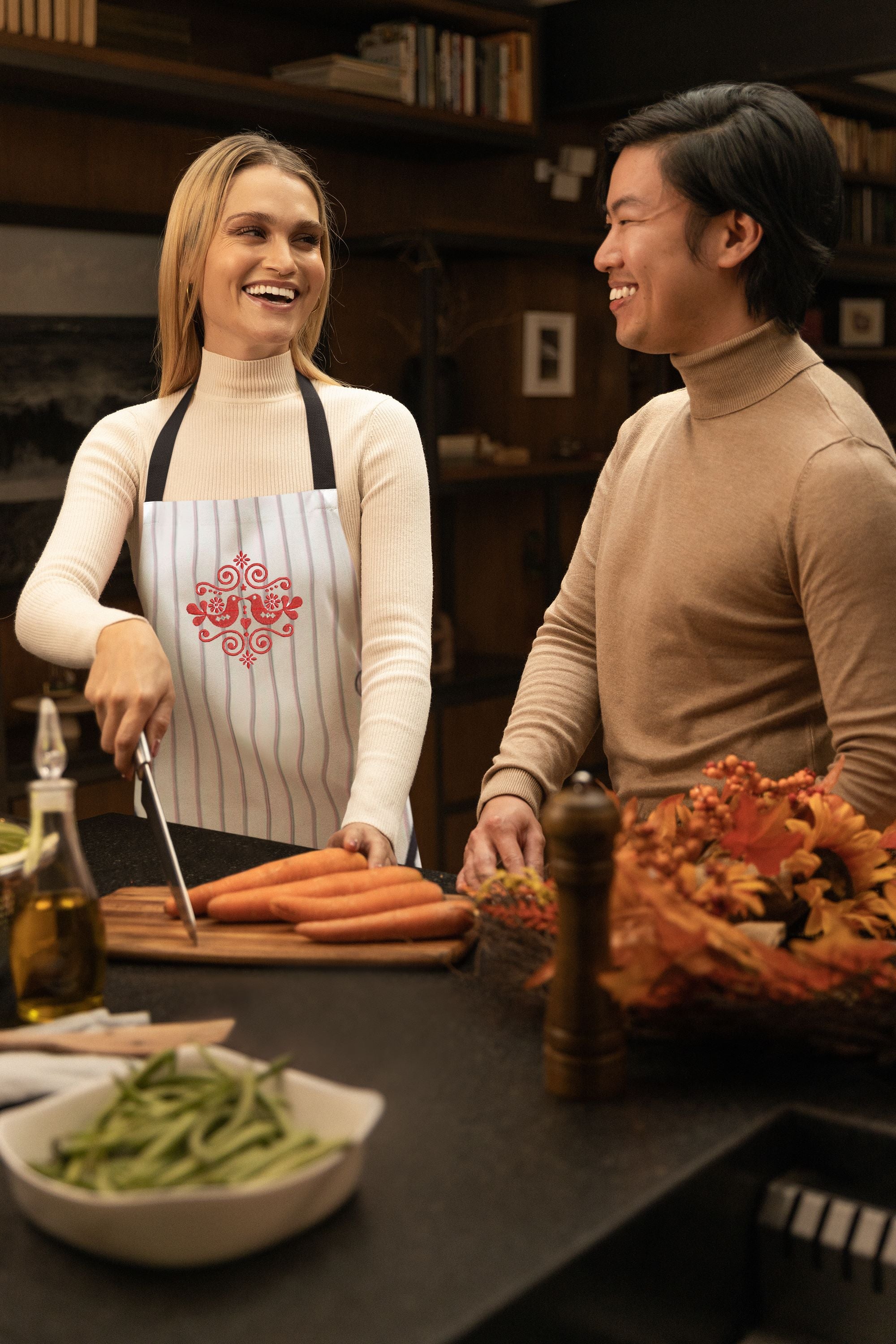 Two people in a kitchen preparing food with carrots and green beans.