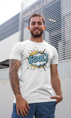A man wearing a white graphic t-shirt with a blue and yellow comic-style 'COOL!' design, standing in front of a modern building with horizontal slats.