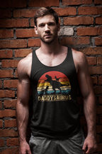 A muscular man wearing a black tank top with a retro sunset graphic and the text 'DADDYSAUROS' stands against a red brick wall background.