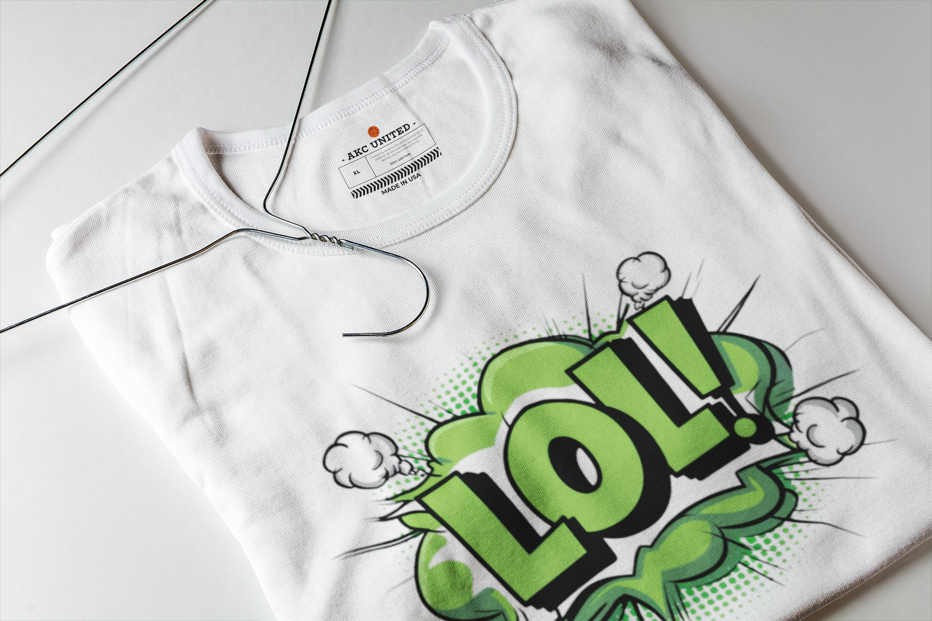 A white short-sleeve t-shirt laid flat on a light gray surface, featuring a bold green and black comic-style 'LOL!' graphic with cloud accents on the front.