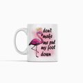 A white ceramic mug featuring a pink flamingo illustration with a flower crown and the text 'don't make me put my foot down' in black script, shown on a clean white background.