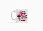 A white ceramic mug featuring a pink flamingo illustration with a flower crown and the text 'don't make me put my foot down' in black script, shown on a clean white background.