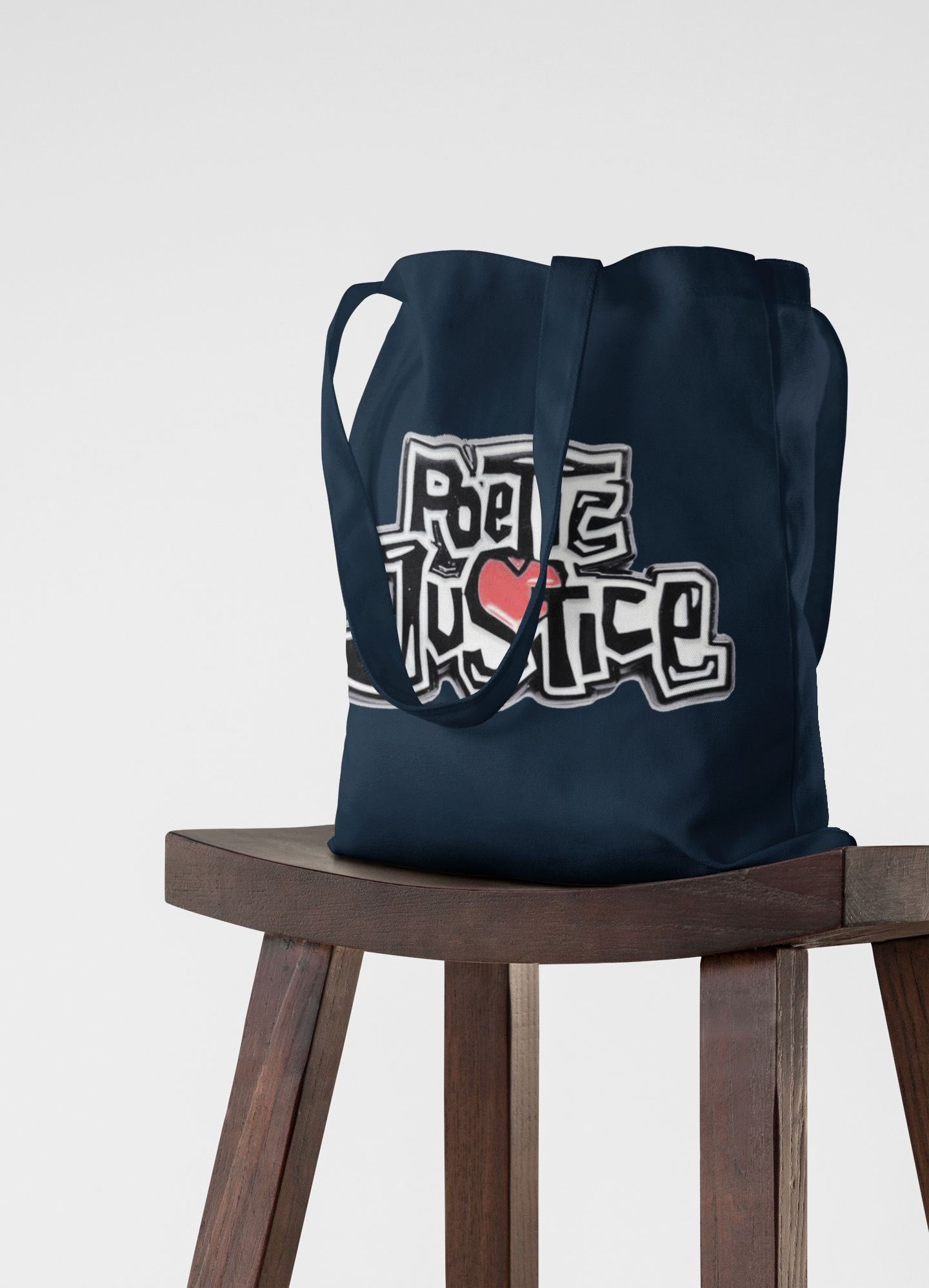 Navy blue tote bag with 'Love Justice' design on a wooden stool against a white background