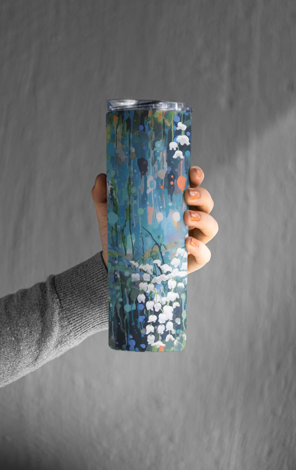 Hand holding a tumbler with a floral design against a gray background