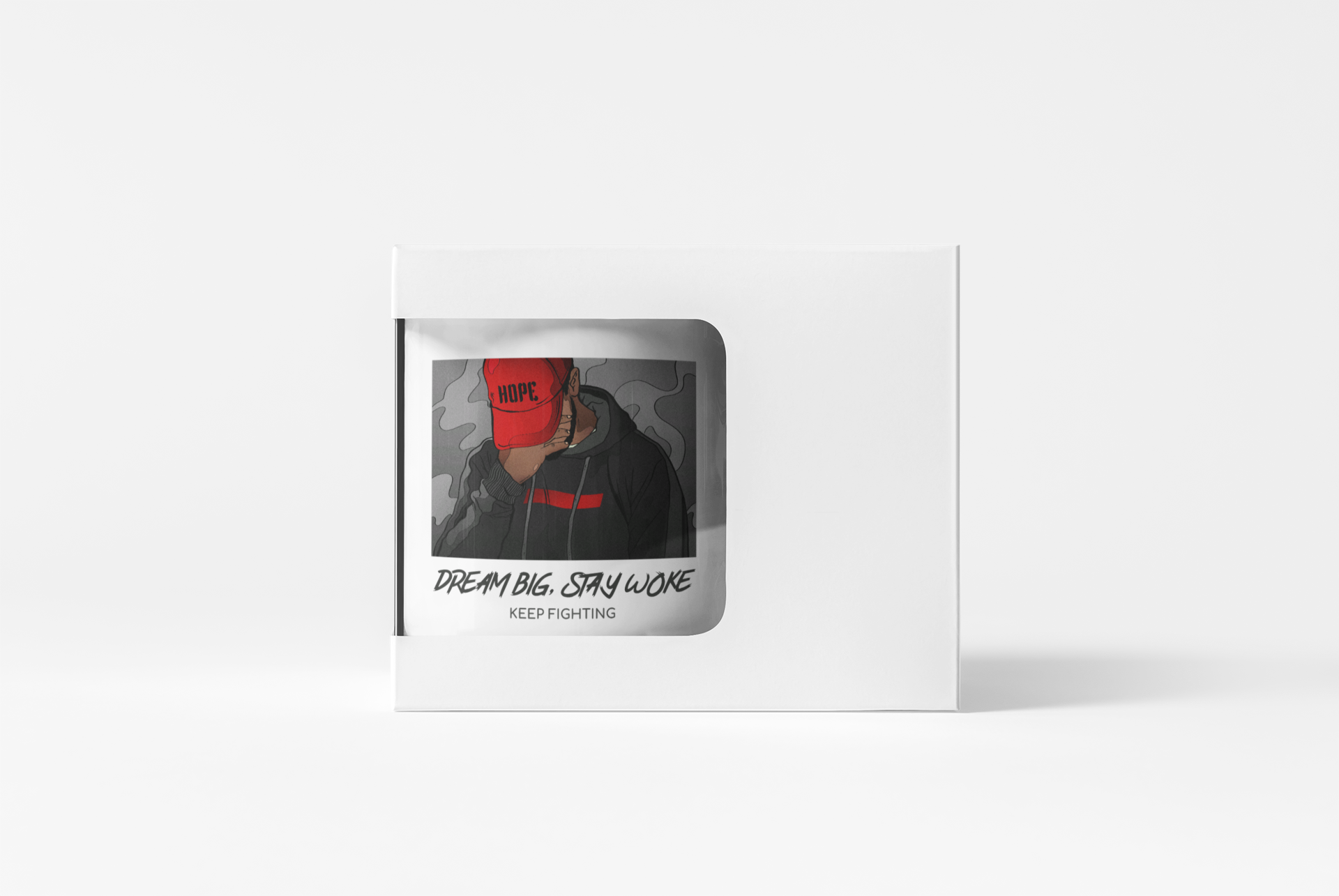 A white square product box with a die-cut window displaying a graphic print of a person in a red cap and black hoodie, with the text 'DREAM BIG, STAY WAKE' and 'KEEP FIGHTING' below.