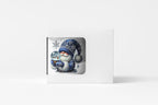 A white rectangular gift box or card holder with a die-cut window showing a winter illustration of a gnome in a blue knit hat and scarf holding a snow globe, set against a clean white background.