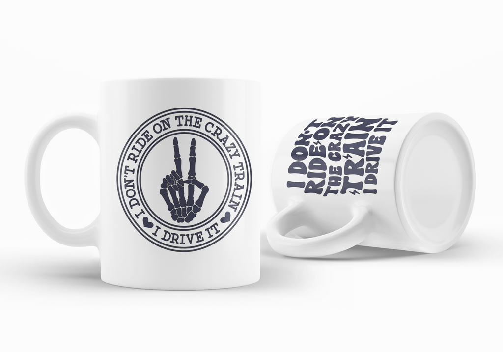 Two white ceramic mugs with dark navy blue printed graphics on a clean white background. One mug is upright and shows a circular graphic of a skeleton hand making a peace sign with the text 'I DON'T RIDE ON THE CRAZY TRAIN I DRIVE IT'.