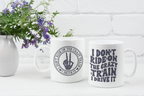 Two white ceramic mugs with dark gray printed text and a hand graphic, displayed on a white surface in front of a white brick wall with a vase of purple flowers on the left.