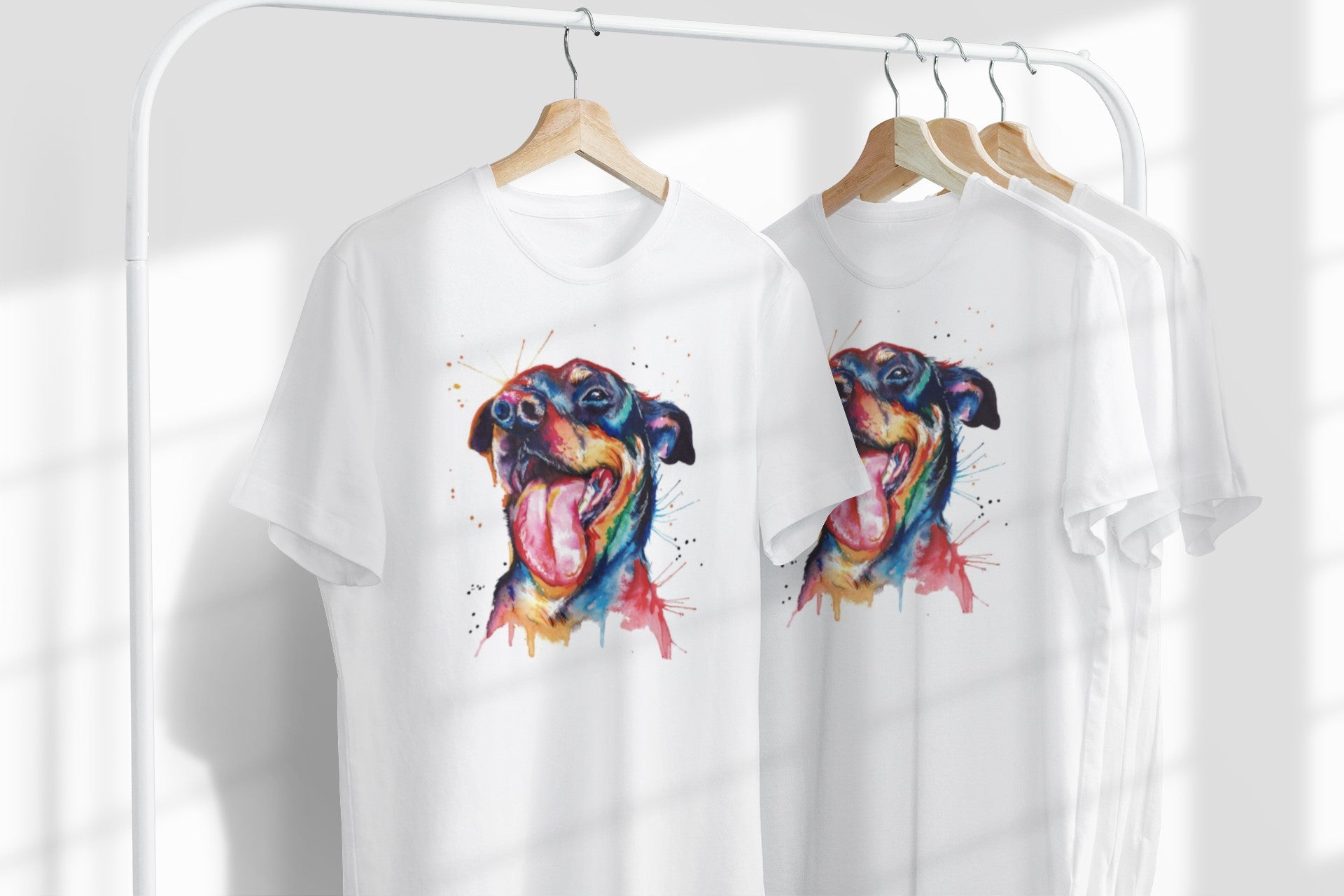 Two white t-shirts with colorful dog illustrations on hangers against a white background