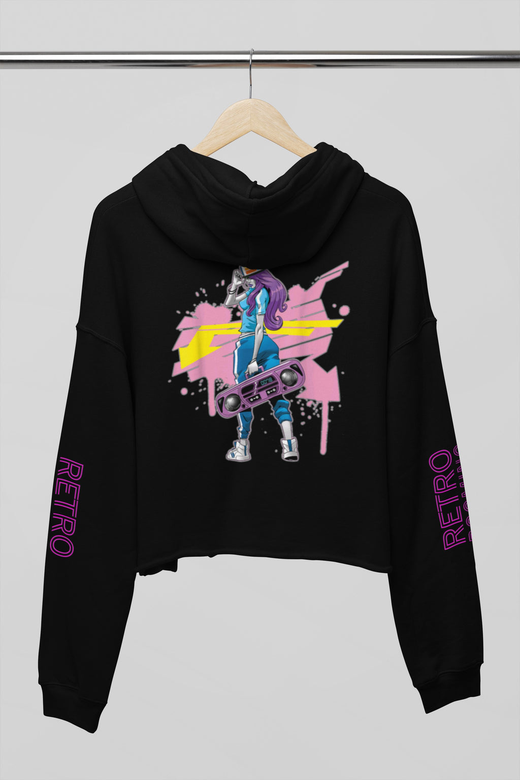 A black cropped hoodie hanging on a wooden hanger against a light gray background. The hoodie features a colorful graphic print on the front with a stylized figure and paint splatters, and the word 'RETRO' printed in purple down both sleeves.