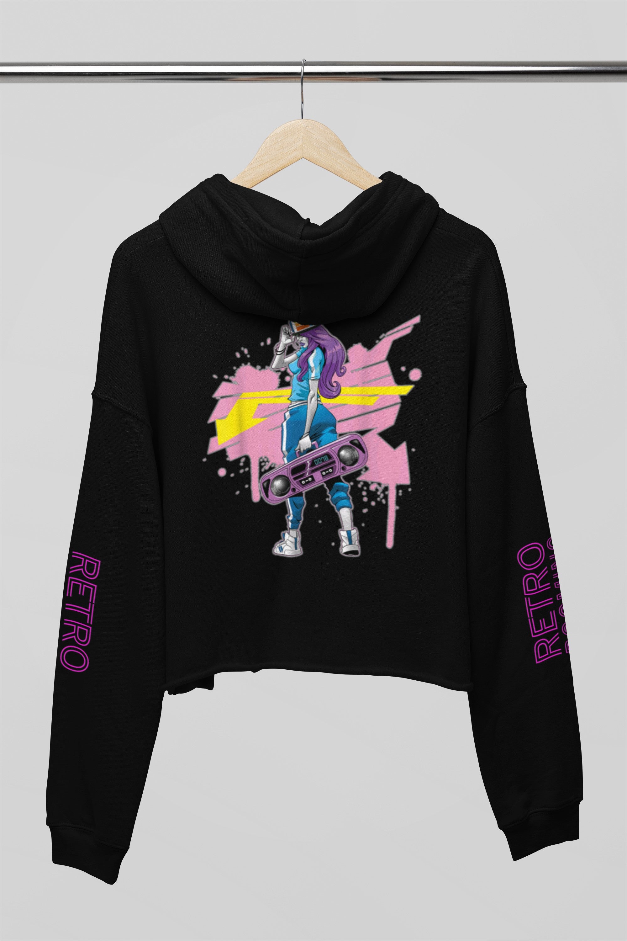A black cropped hoodie hanging on a wooden hanger against a light gray background. The hoodie features a colorful graphic print on the front with a stylized figure and paint splatters, and the word 'RETRO' printed in purple down both sleeves.
