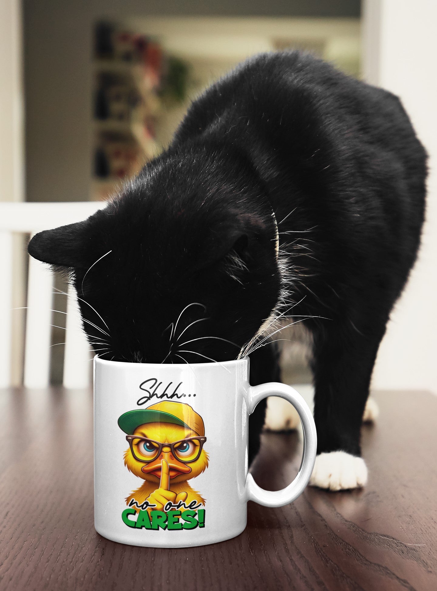Black cat interacting with a mug featuring a duck graphic and text on a wooden table.