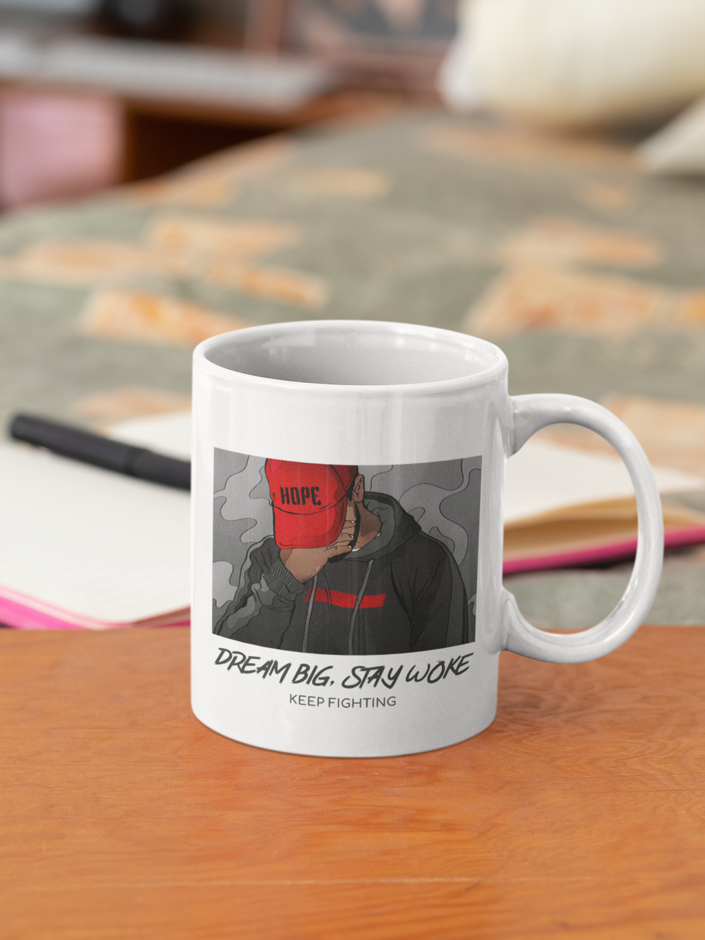 A white ceramic coffee mug with a printed graphic of a person wearing a red cap and the text 'DREAM BIG. STAY WOKE.