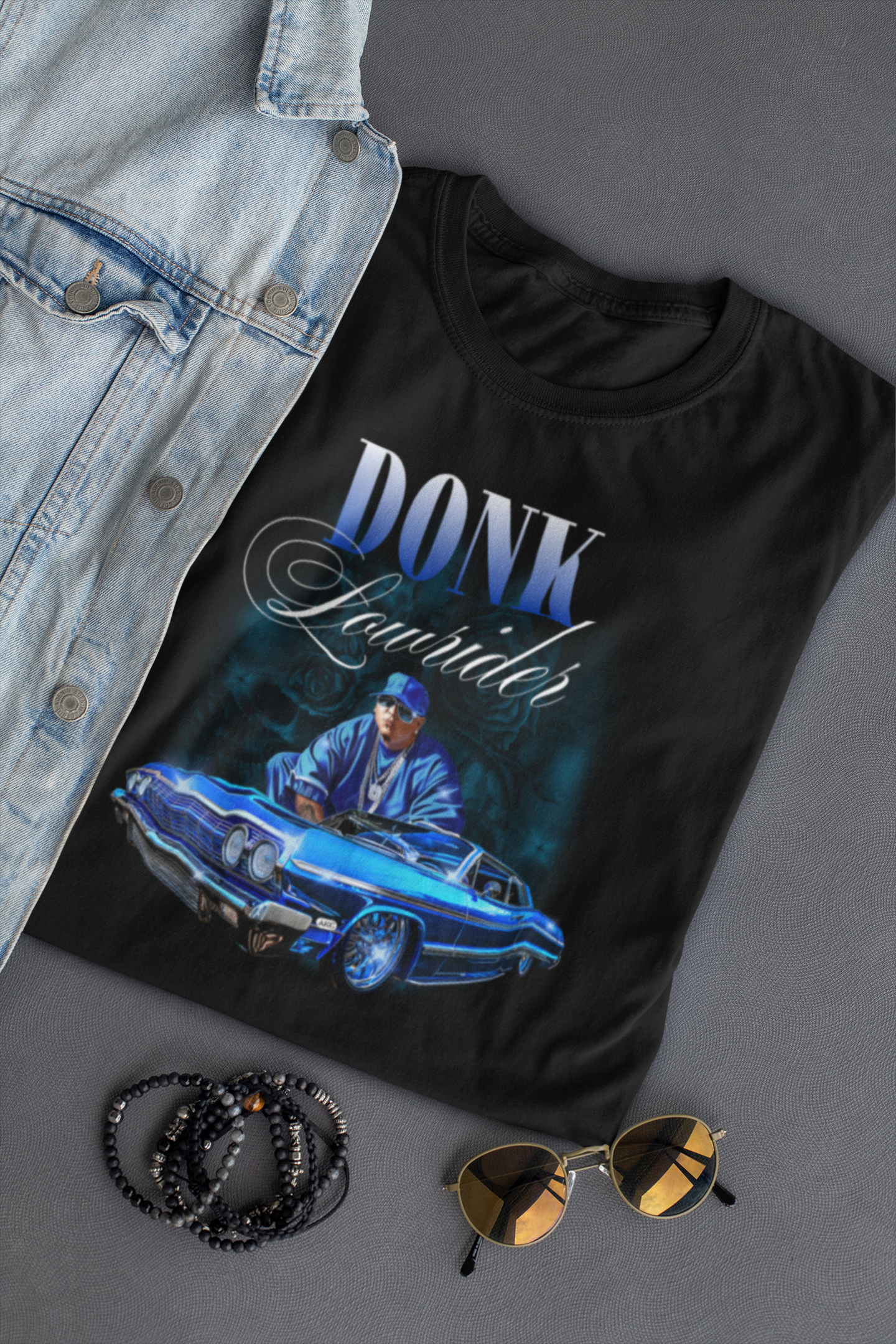 Black t-shirt with 'Donk Fender' graphic, denim jacket, sunglasses, and beads on a gray surface