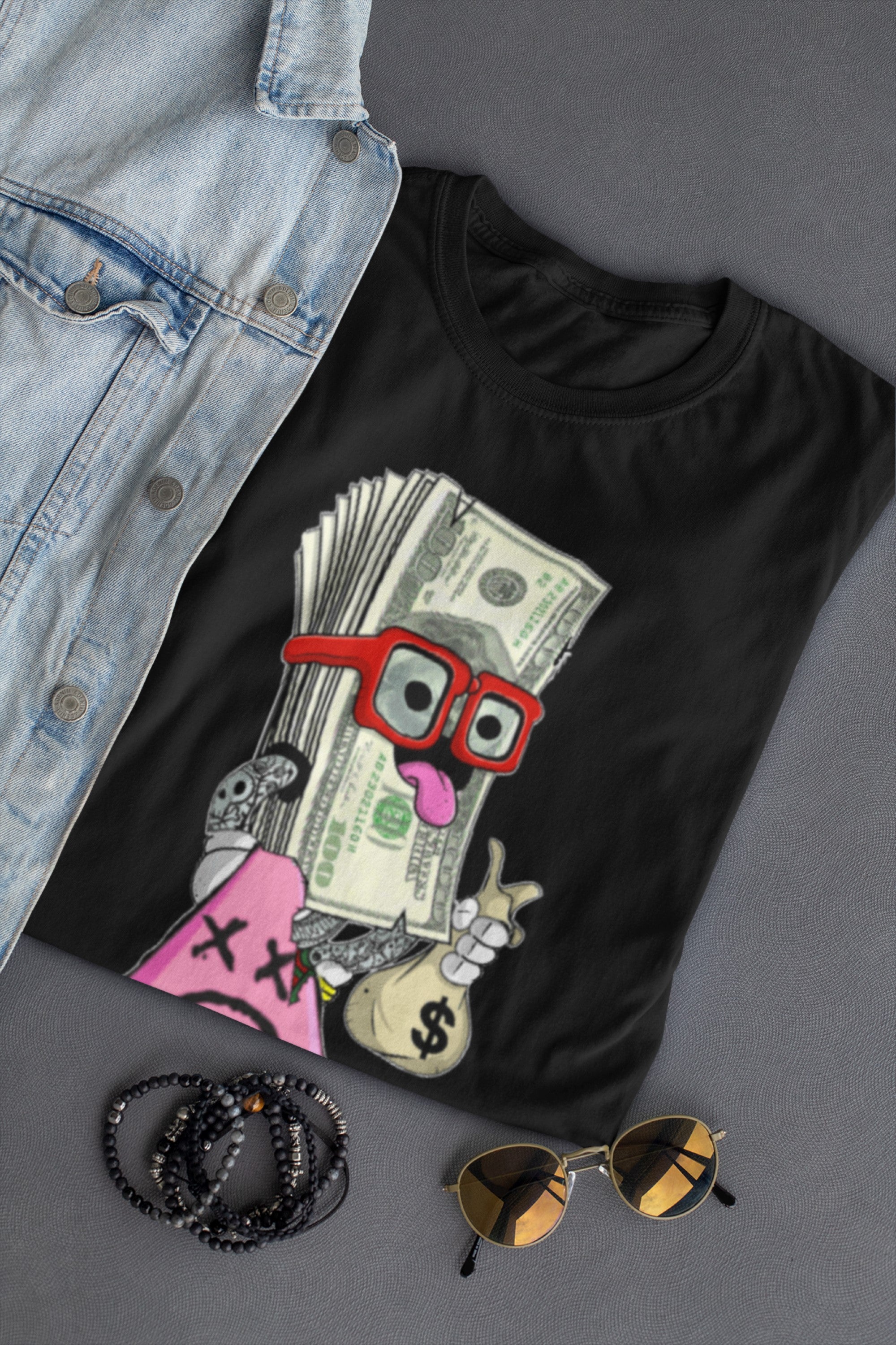 Black t-shirt with money-themed graphic, denim jacket, sunglasses, and bracelets on a gray surface
