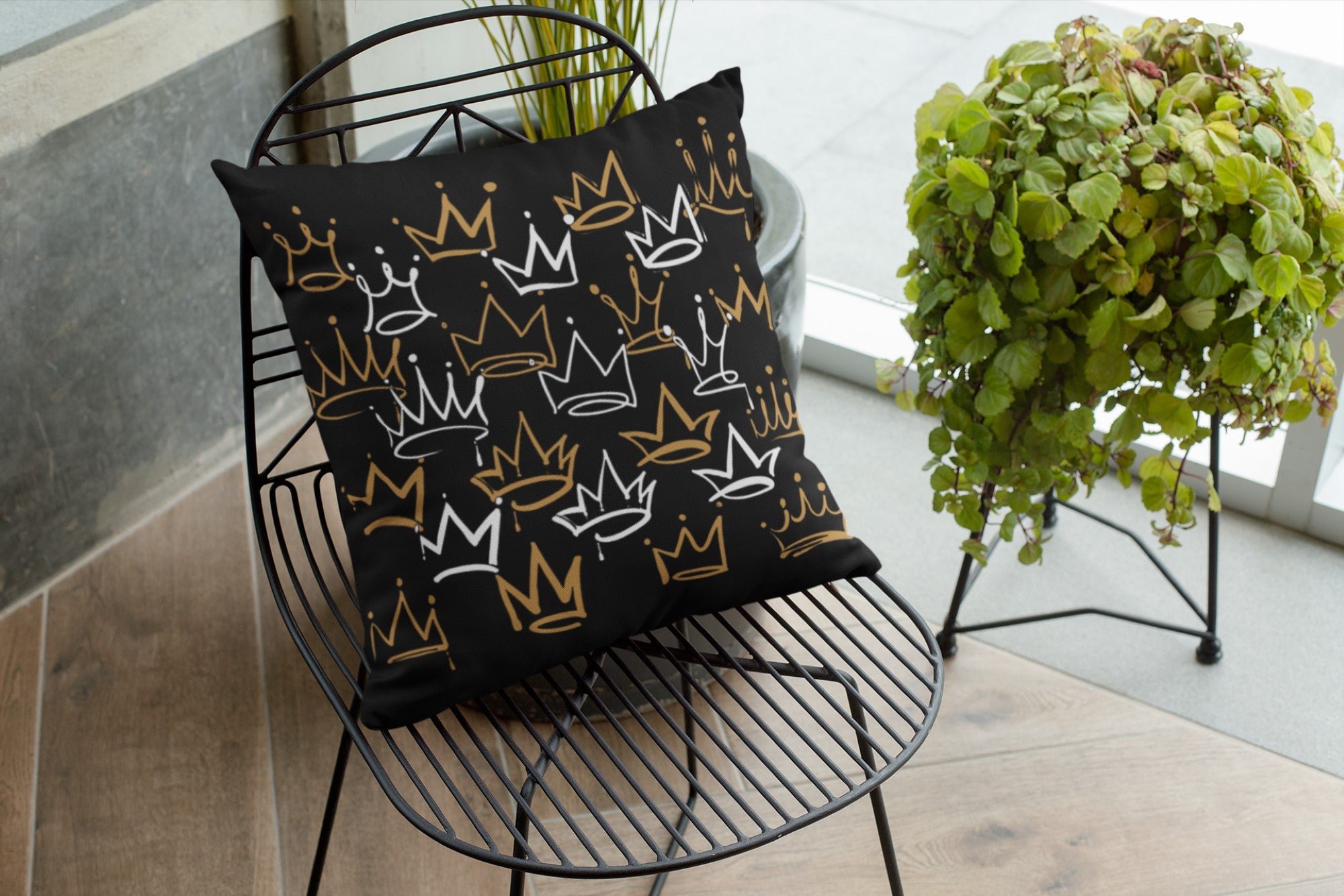 Decorative pillow with crown patterns on a black wire chair indoors.