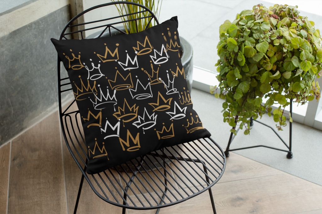Decorative pillow with crown patterns on a black wire chair next to a potted plant.