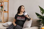 Woman sitting on a couch holding a mug with 'ANYA KNOWS' shirt in a cozy living room.