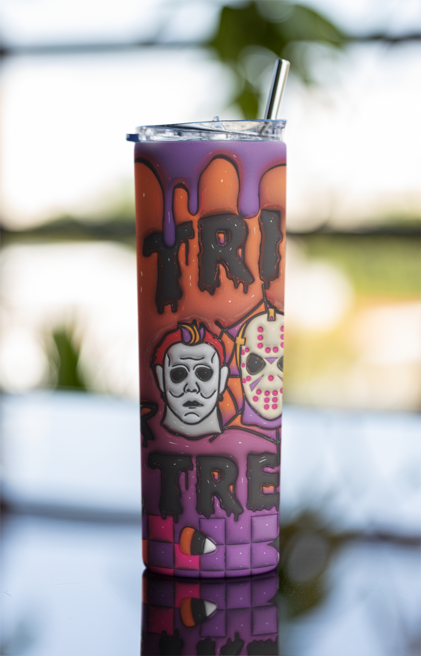 A purple and orange Halloween-themed tumbler with a clear lid and metal straw, featuring horror character graphics and the words 'TRICK' and 'TREAT'.