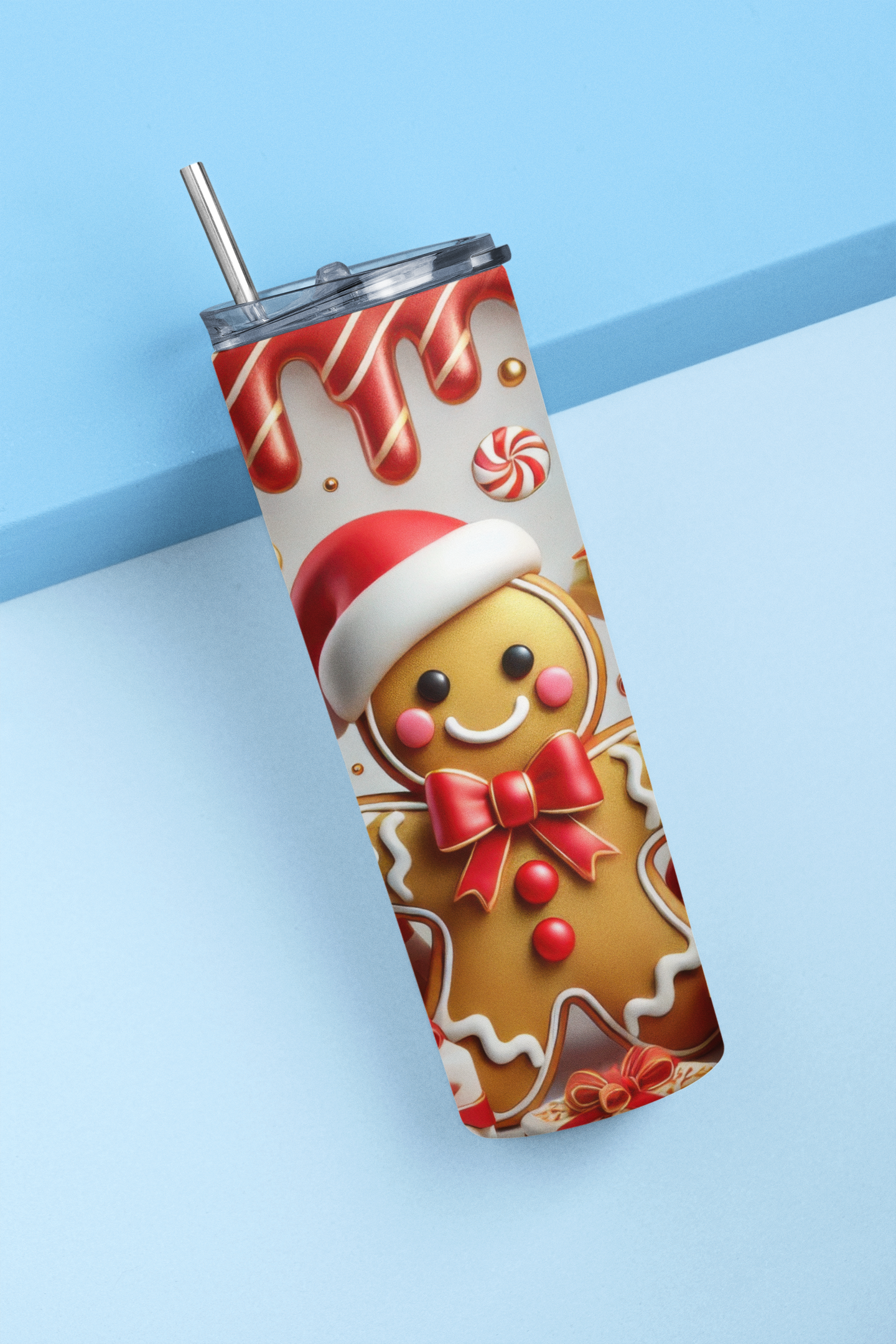 A stainless steel tumbler with a clear lid and metal straw, featuring a festive Christmas gingerbread man print, set against a light blue background.
